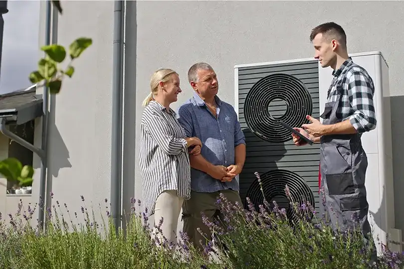 Ein Techniker bespricht mit einem Paar die Funktionen einer externen Wärmepumpe.
